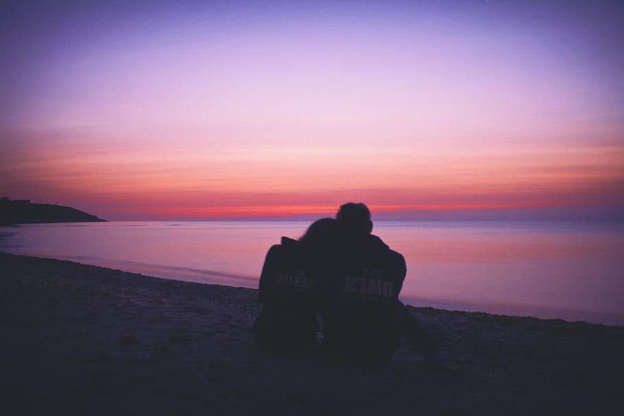 man and woman hugging each other on seashore during sunset, silhouette of couple sitting on seashore