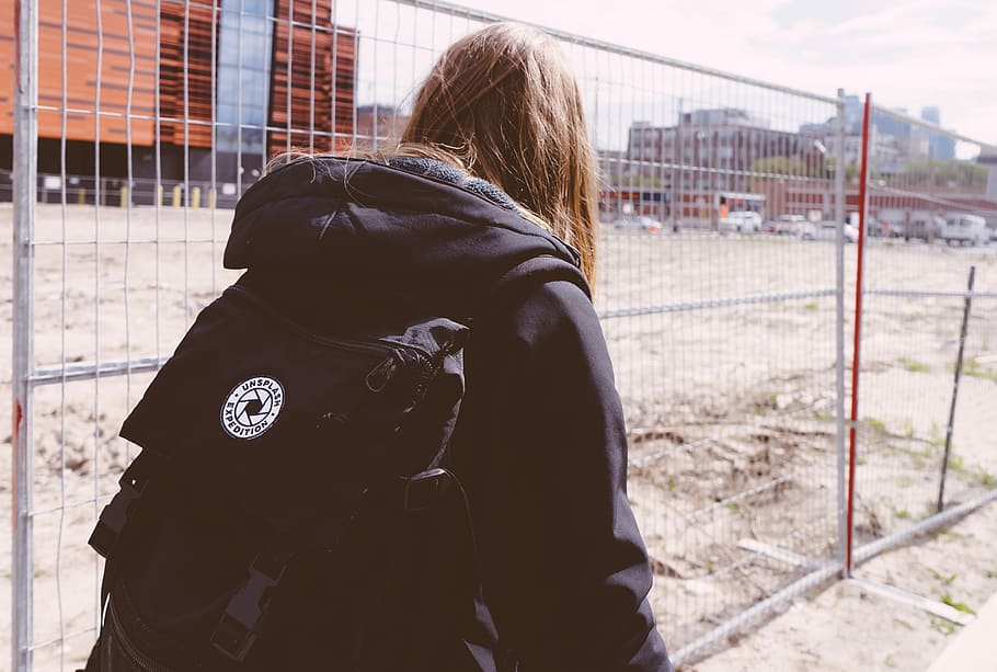 person wearing black jacket walking near fence, person in black hoodie and backpack HD wallpaper