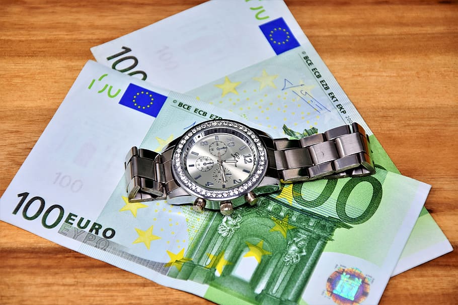 chronograph watch on 100 Euro banknote on brown wooden surface