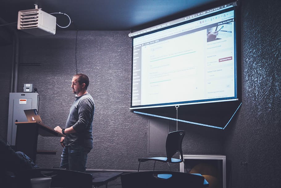 person standing in front of brown lectern, man in front of laptop computer HD wallpaper