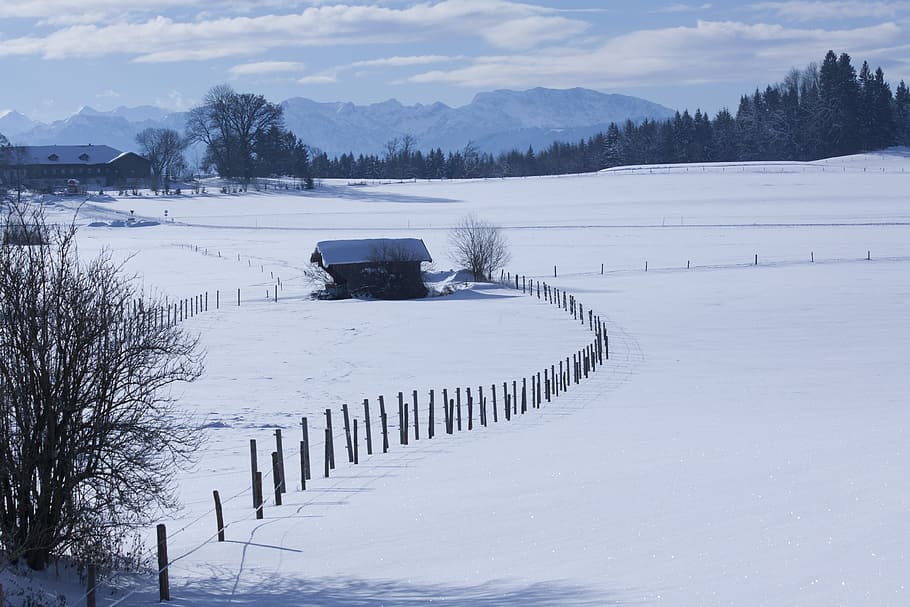 black wooden house in field covered with snow viewing mountain at daytime