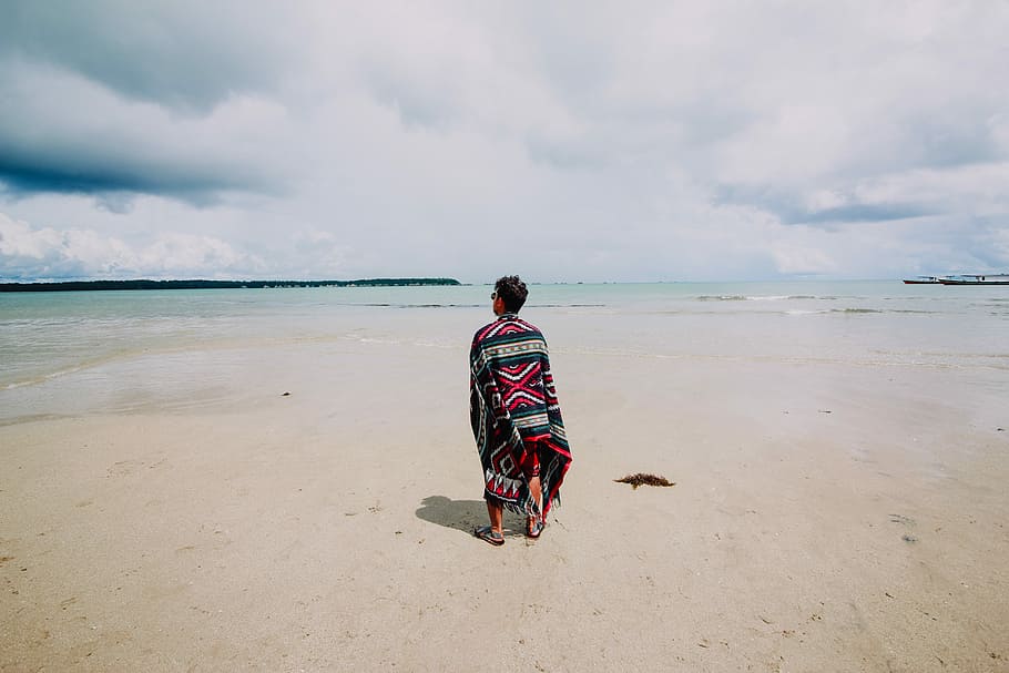 man wearing red and green scarf facing body of water, man standing in front on beach during daytime HD wallpaper