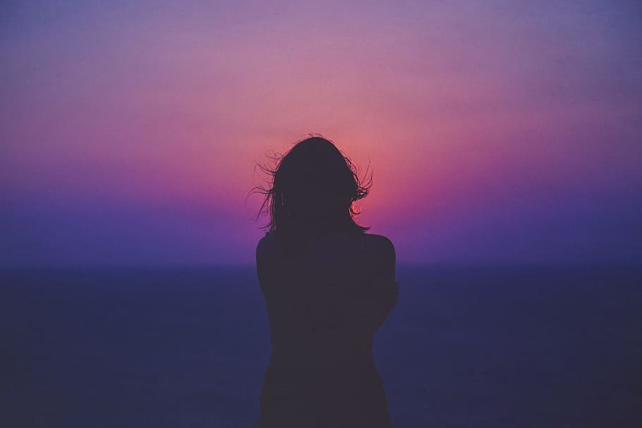silhouette of a woman with pink and purple sky, photo of silhouette of woman standing near beach