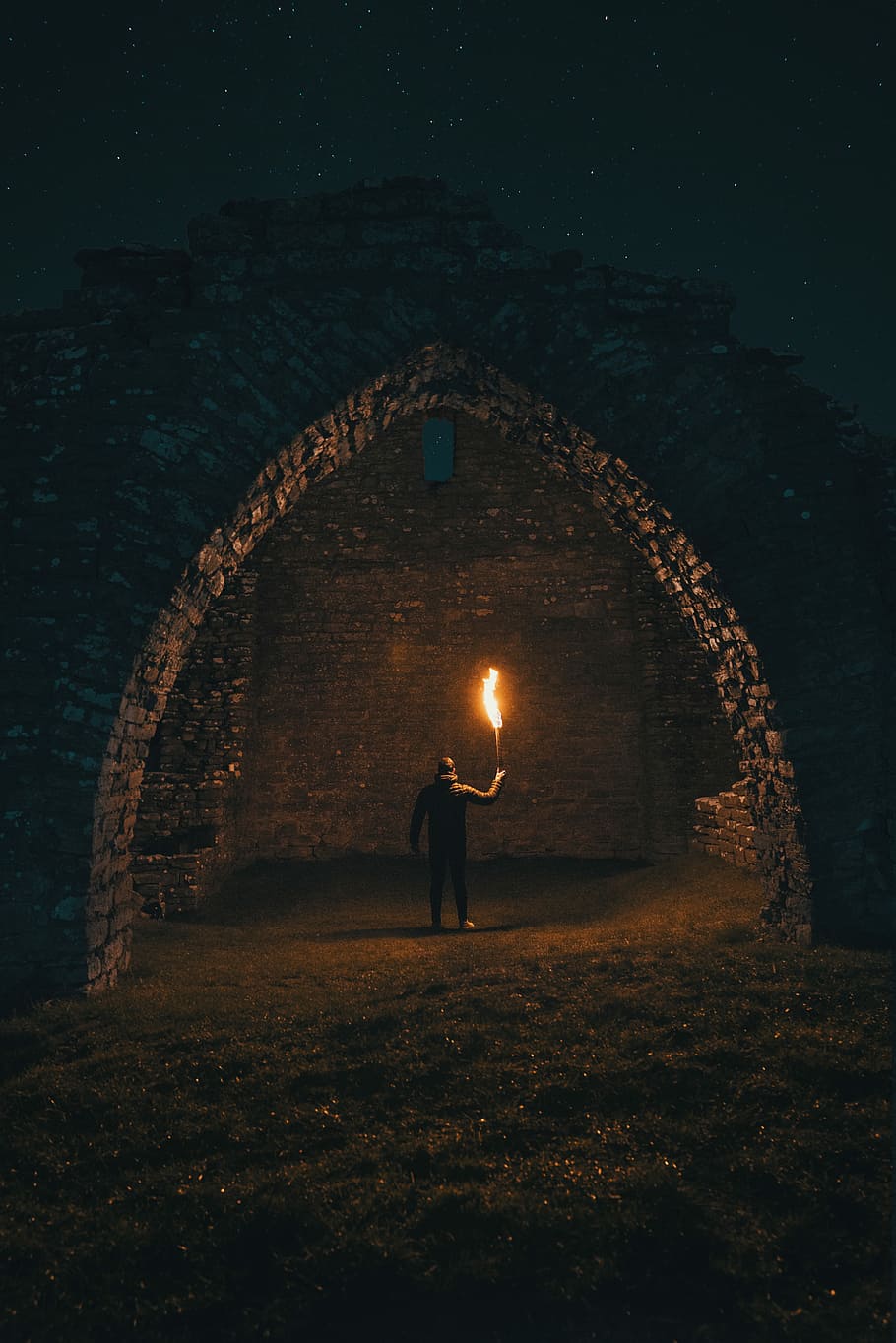 person holding torch in building interior, man carrying torch inside arc-shaped brick shed