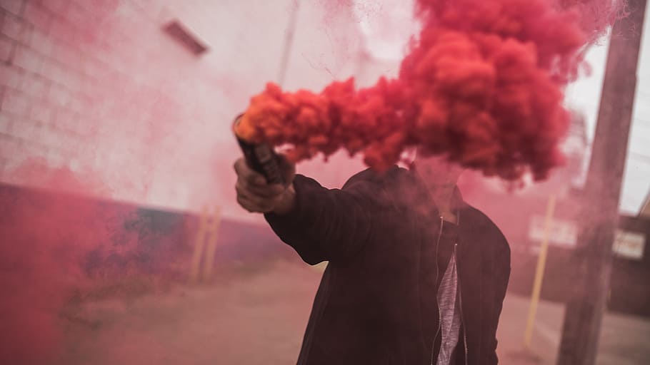 man holding red smoke grenade, guy, color, wall, bricks, post