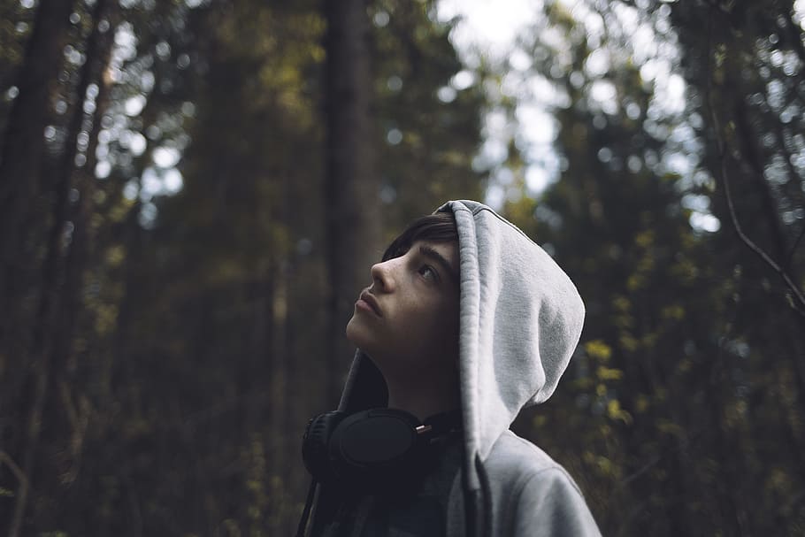 shallow focus photo of man looking at trees, man wearing hoodie and headphones