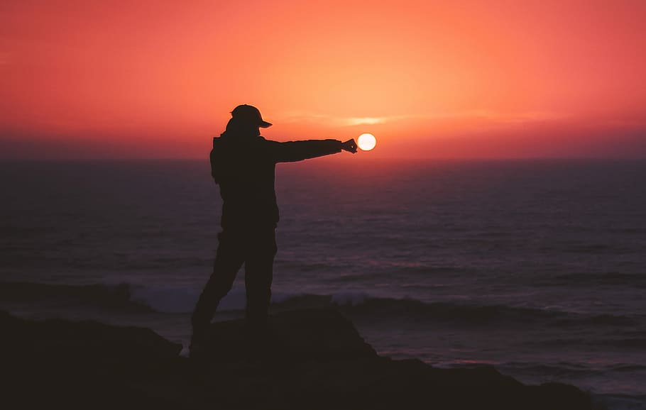 person standing on rock near body of water, silhouette photography of person standing in front of body of water during golden hour HD wallpaper