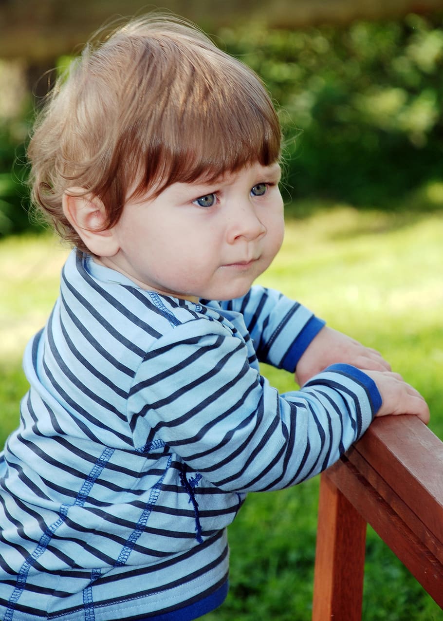toddler holding on brown wooden rack, small child, boy, skeptical