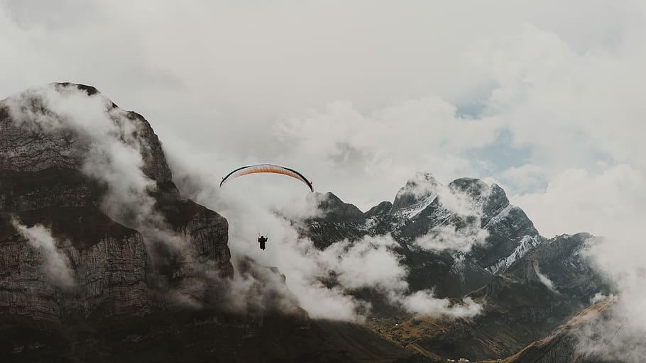person on parachute near the mountain, person paragliding near gray mountains under cloudy sky during daytime HD wallpaper