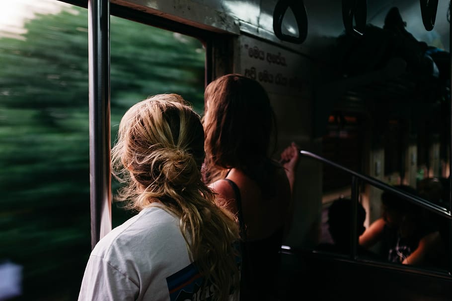 two person standing on train window, women standing inside train