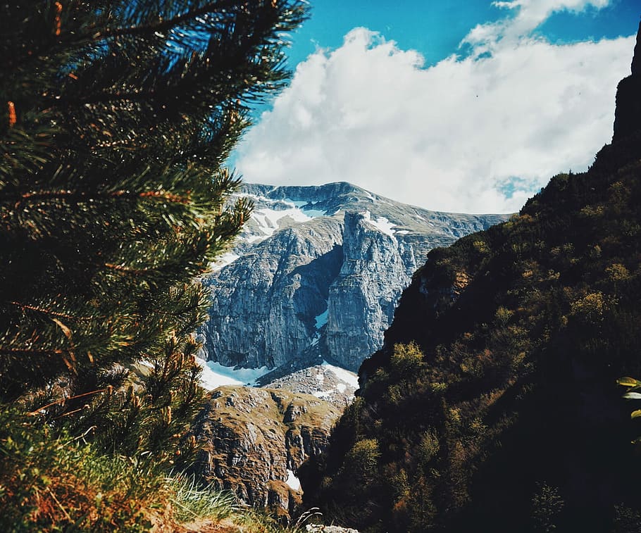 landscape photography of mountain ranges under party cloudy skies, photo of green leaf plant in front of rocky mountain during daytime HD wallpaper