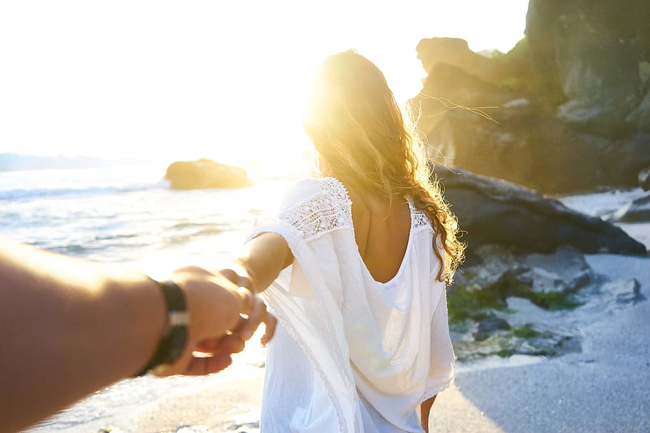 person holding woman's hand beside sea while facing sunlight, person holding a woman hand on seashore