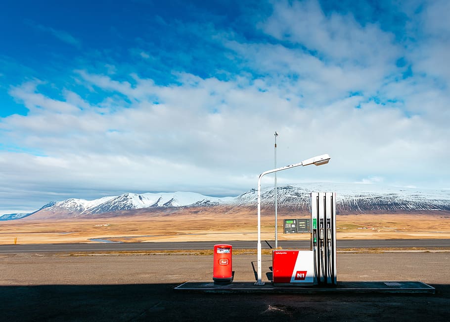 empty gas station near empty road facing snow capped mountain at daytime, white lamp post on road