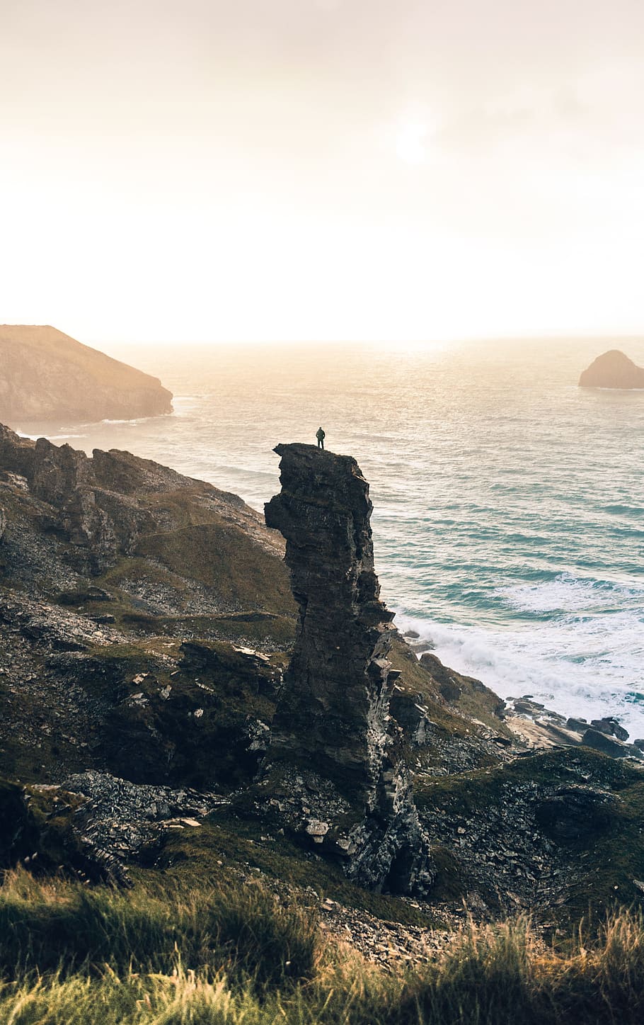 man standing on rock cliff near body of water, person standing on rock near sea HD wallpaper