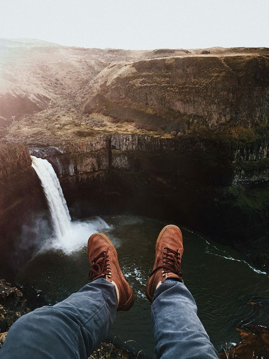 person's pair of brown shoes, person sitting on ledge looking at the waterfalls HD wallpaper