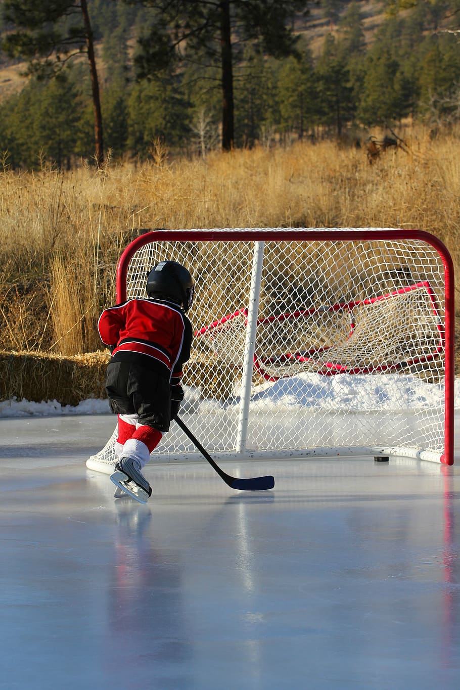 kid playing hockey, outdoor rink, net, goal, hockey stick, ice hockey