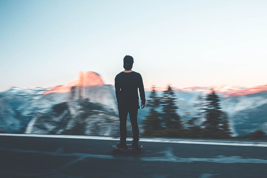 man standing on cruiser board, man riding on skateboard near pine trees and mountain HD wallpaper