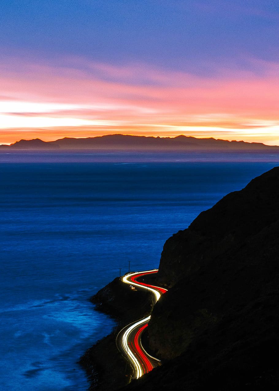time-lapse photography of cliff road during golden hour, ocean under black sky