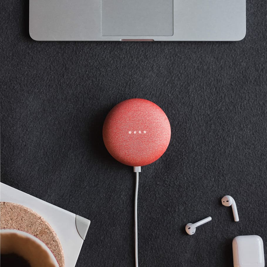 flat lay photography of coral Google Home Mini on black surface beside Apple AirPods, red Google Mini speaker on black cloth HD wallpaper