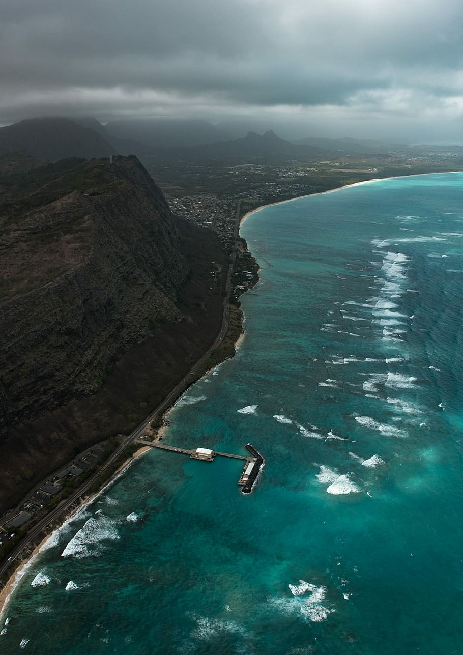 aerial photo of beach dock near cliff, rock cliff near body of water under cloudy skies, HD wallpaper