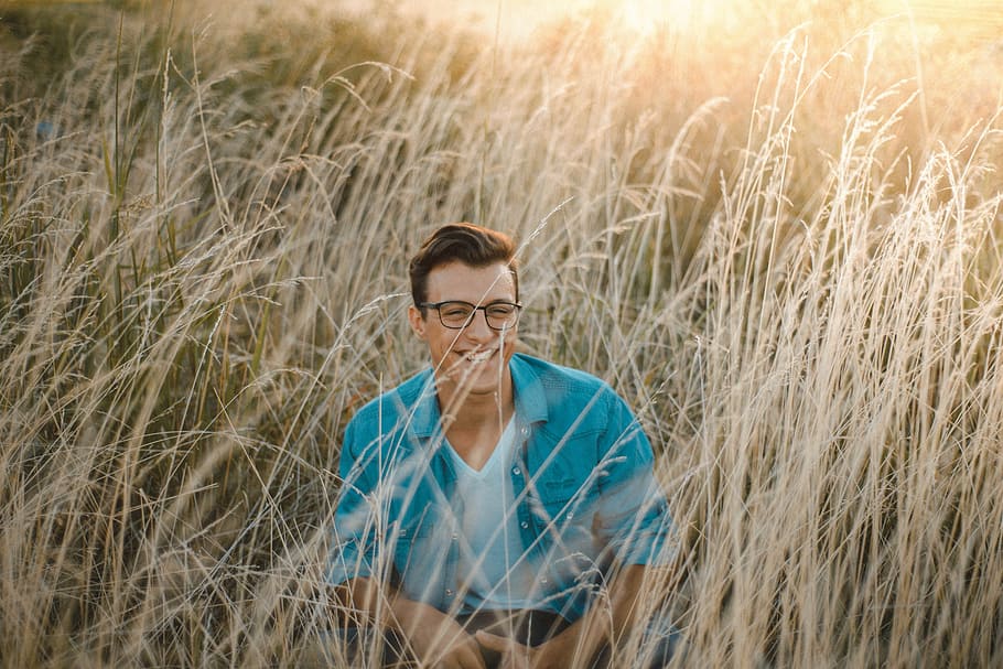 man sitting surrounded by grass during daytime, man seating on ground surrounded by grass HD wallpaper