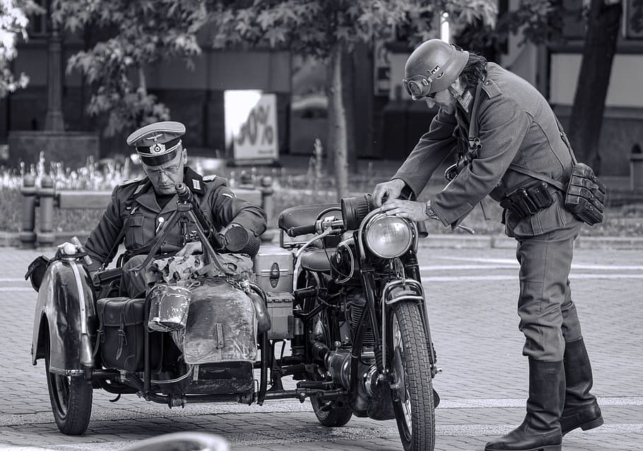 grayscale photo of man on motorcycle with side car near man standing