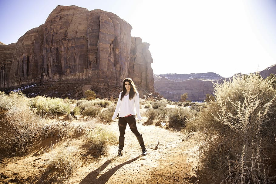 woman standing on green grass near brown mountain during daytime, woman wearing white dress shirt standing near brown cliff HD wallpaper