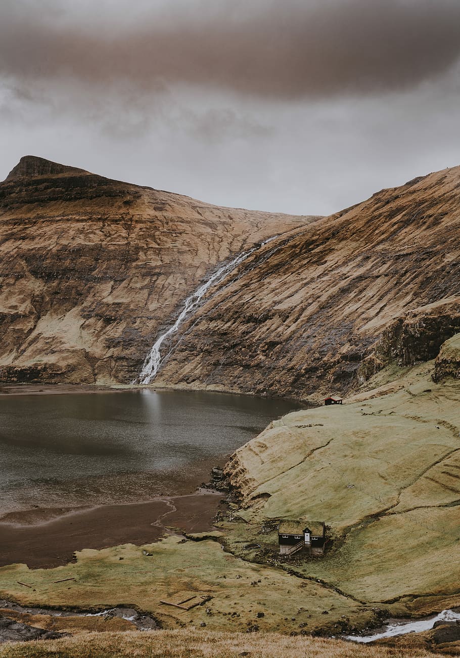 brown rock mountain with waterfalls, person taking photo of lake HD wallpaper