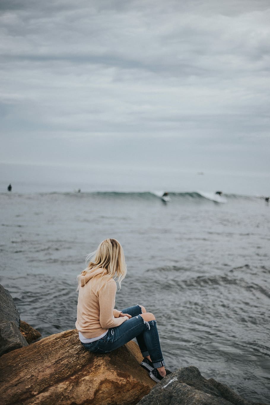 woman sitting on rock near body of water, woman sitting on brown rock formation looking at sea during daytime HD wallpaper