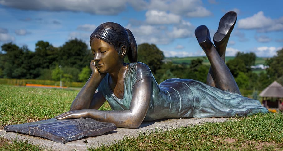 girl lying on her stomach while reading book statue, bronze, outdoor