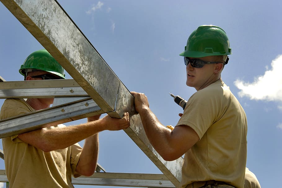 man wearing beige shirt and green safety helmet holding white steel bars, HD wallpaper