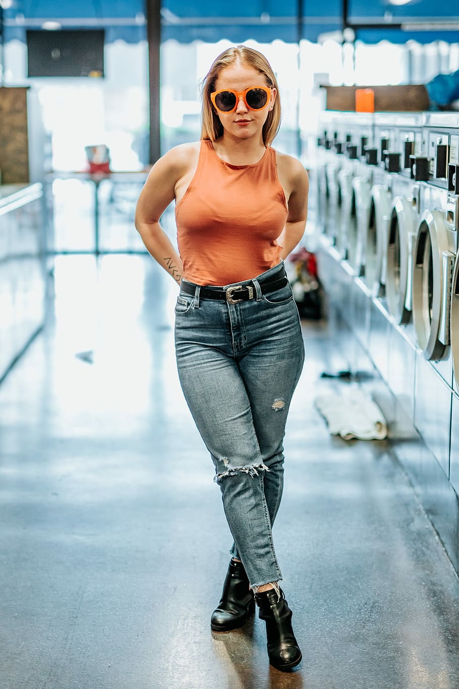 woman wearing orange sleeveless top and blue denim jeans standing near front-load laundry appliances, HD wallpaper