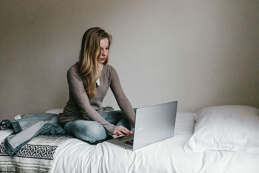 woman typing on MacBook Pro while sitting on bed in room, woman sits in bed front of laptop