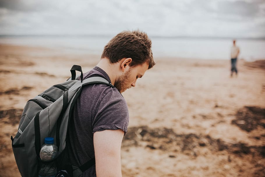 man in gray shirt and backpack beside beach shore during daytime, selective focus photography of man wearing gray backpack at beach HD wallpaper