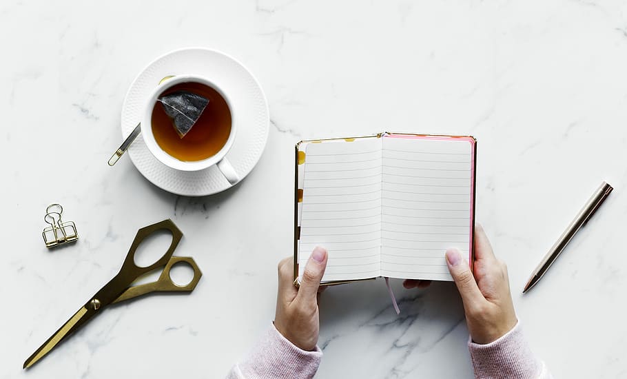 person holding white notebook near white ceramic cup, tea, table HD wallpaper