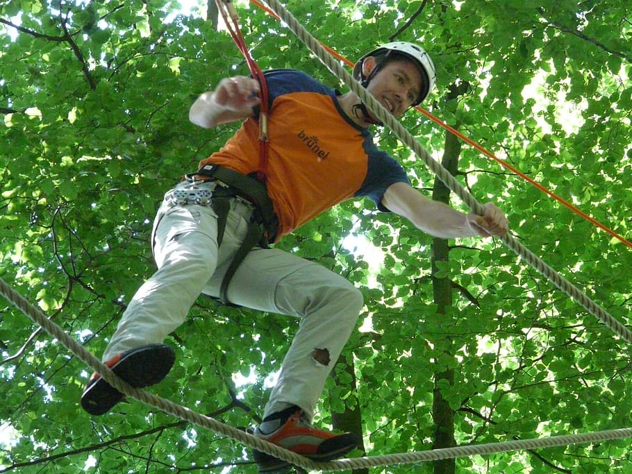 selective focus photo of a man wearing safety harness walking on rope surrounded by trees during daytime