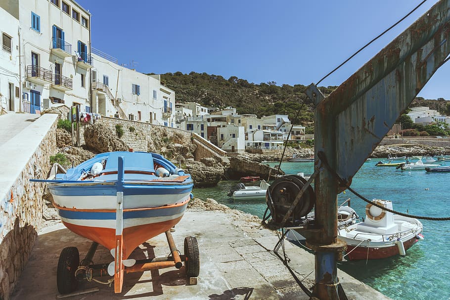 white and blue speedboat parked near the building, blue, orange, and white boat beside body of water HD wallpaper