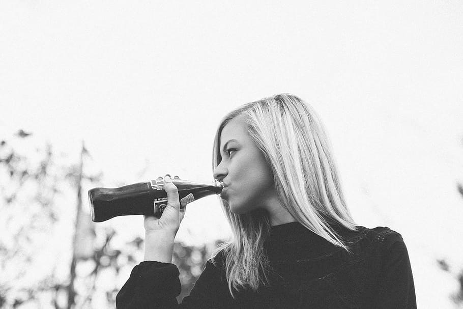 greyscale photography of woman in sweater drinking coca-cola in bottle during daytime HD wallpaper