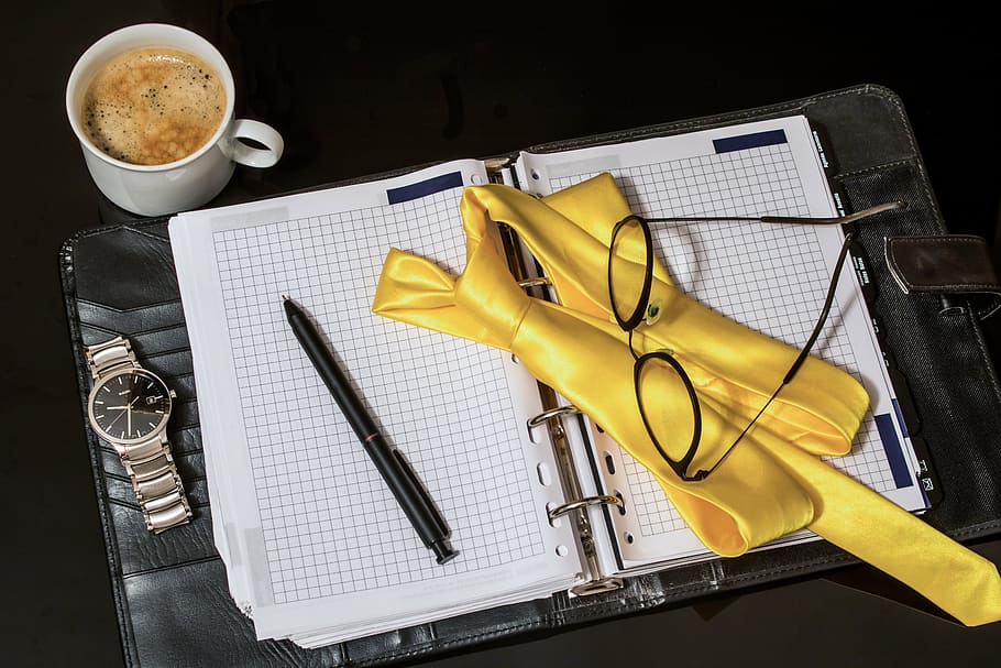 eyeglasses on white graphing notebook, agenda, tie, pen, men's watch