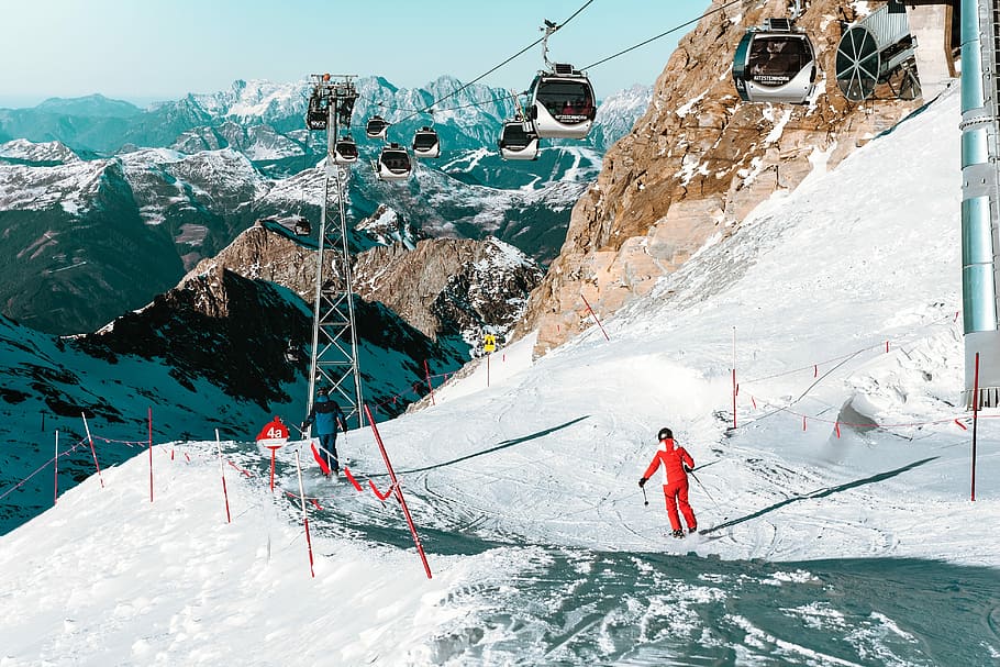 person doing some ski on under cable car, man standing on snowfield below the cable cart during day time HD wallpaper