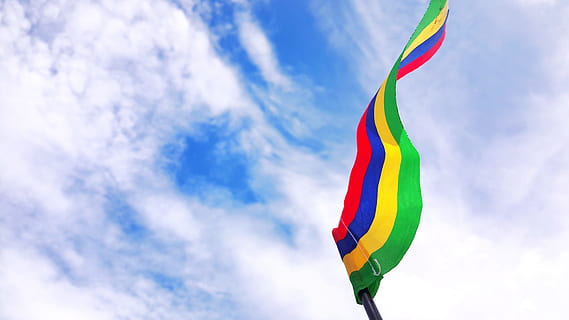 red, blue, yellow, and green striped flag under blue sky, low-angle photography of red, blue, yellow, and green striped flag HD wallpaper