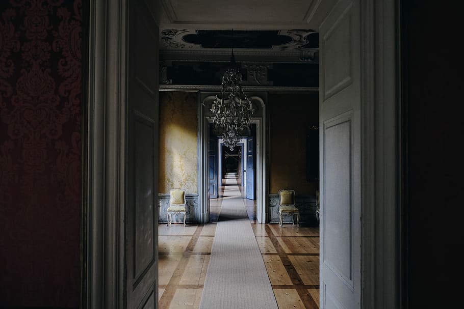 opened white wooden door near chandelier, two brown area rugs beside white door