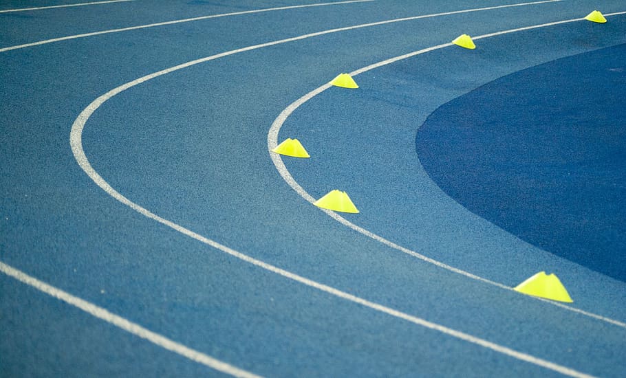 blue curved track field at daytime, track field, cones, lines