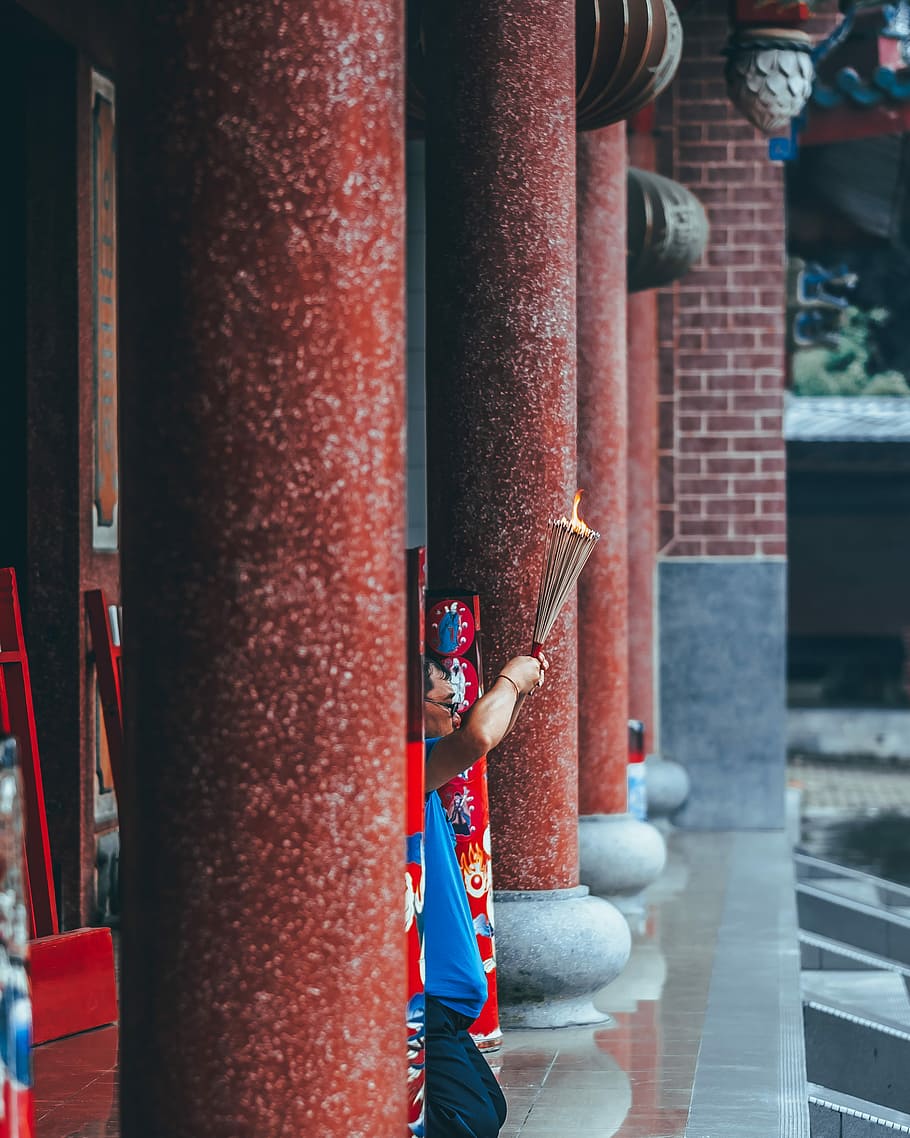 man kneeling while holding incense outdoors, person holding sticks while hiding on gray concrete pole HD wallpaper