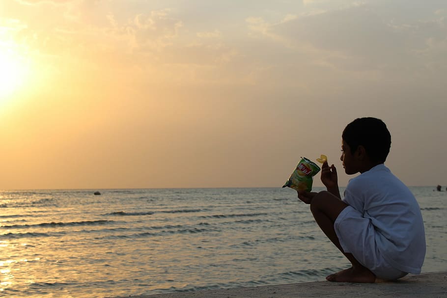 boy squatting in front calm body of water at sunset, action camera HD wallpaper