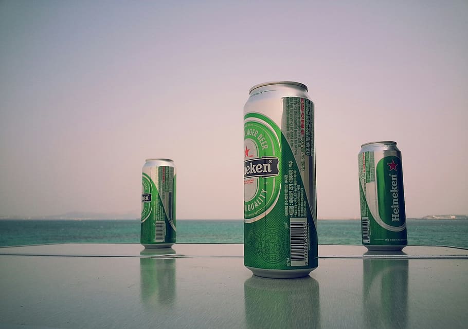 three green-and-gray Heineken beverage cans, beer, sea, no people