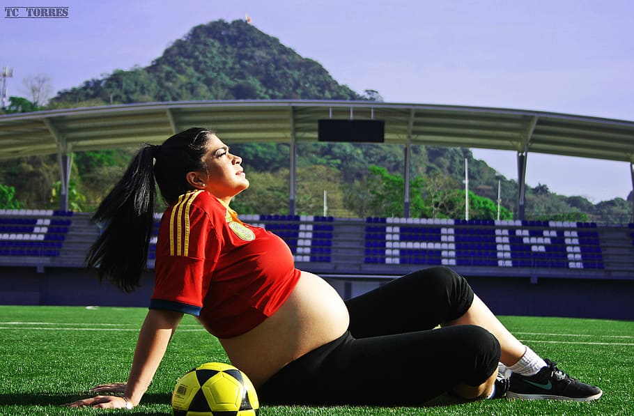 woman sitting on grass field, pregnancy, football, maracana stadium