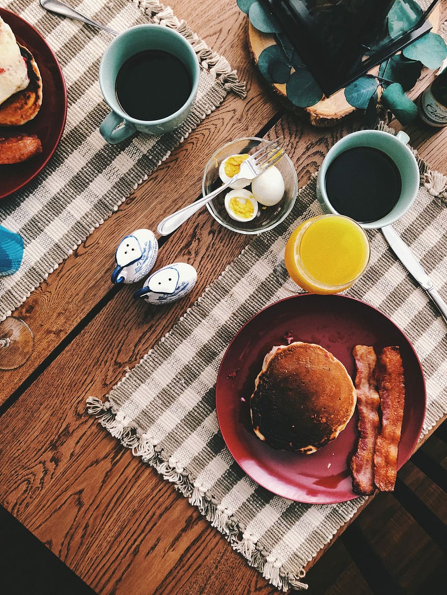 baked bread on round red ceramic plate near glass of orange juice, cup of coffee, and boiled eggs, pancake and bacon strips HD wallpaper
