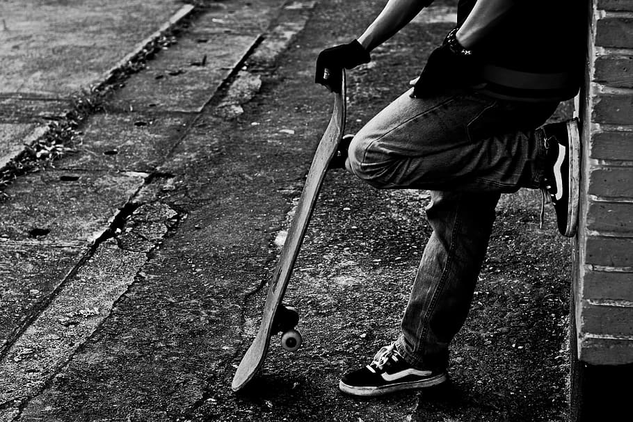 grayscale photo of man holding skateboard while leaning on wall, HD wallpaper