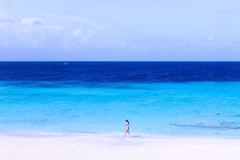 woman walking on seashore, woman in swimsuit walking on white sand beach shore during daytime HD wallpaper